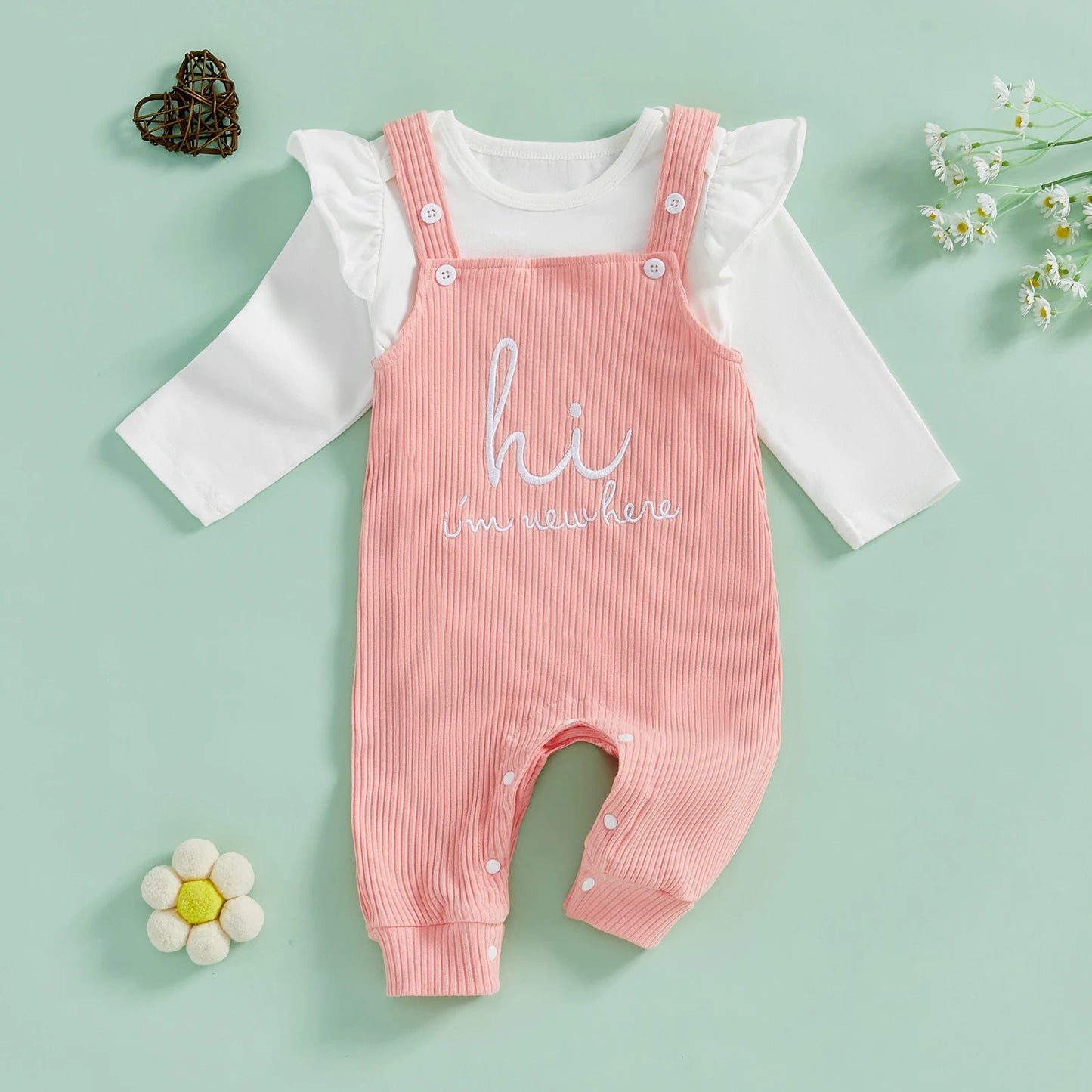 Flat lay of baby girl outfit set – white long sleeve romper and pink ribbed overalls with embroidered slogan